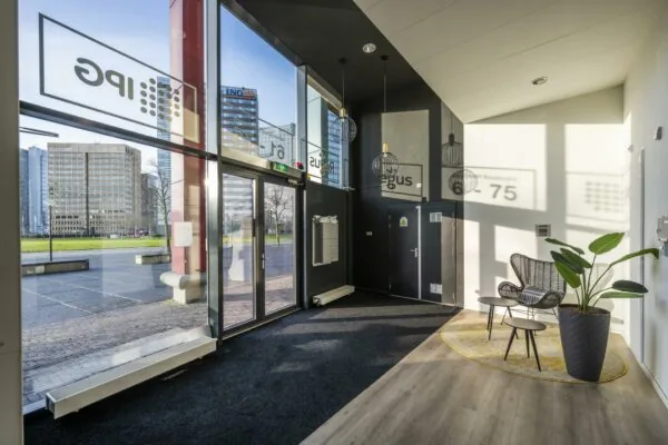 Moderne entreehal van een kantoorpand aan de Johan Cruijff Boulevard met grote ramen, zitgedeelte en uitzicht op omliggende kantoorgebouwen.